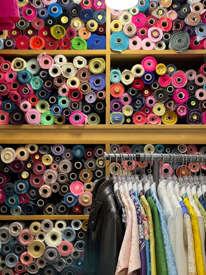 who-we-are Colorful fabric rolls above clothes rack in tailor shop, capturing textile diversity.
