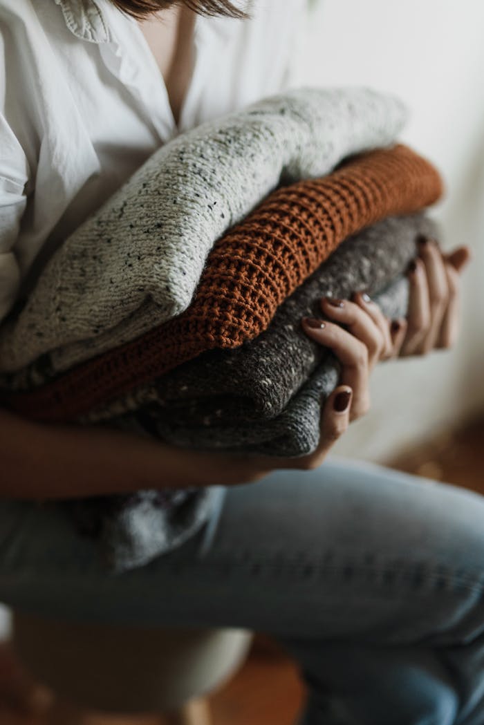 services-04 Close-up of a person holding a stack of folded sweaters, evoking warmth and comfort.
